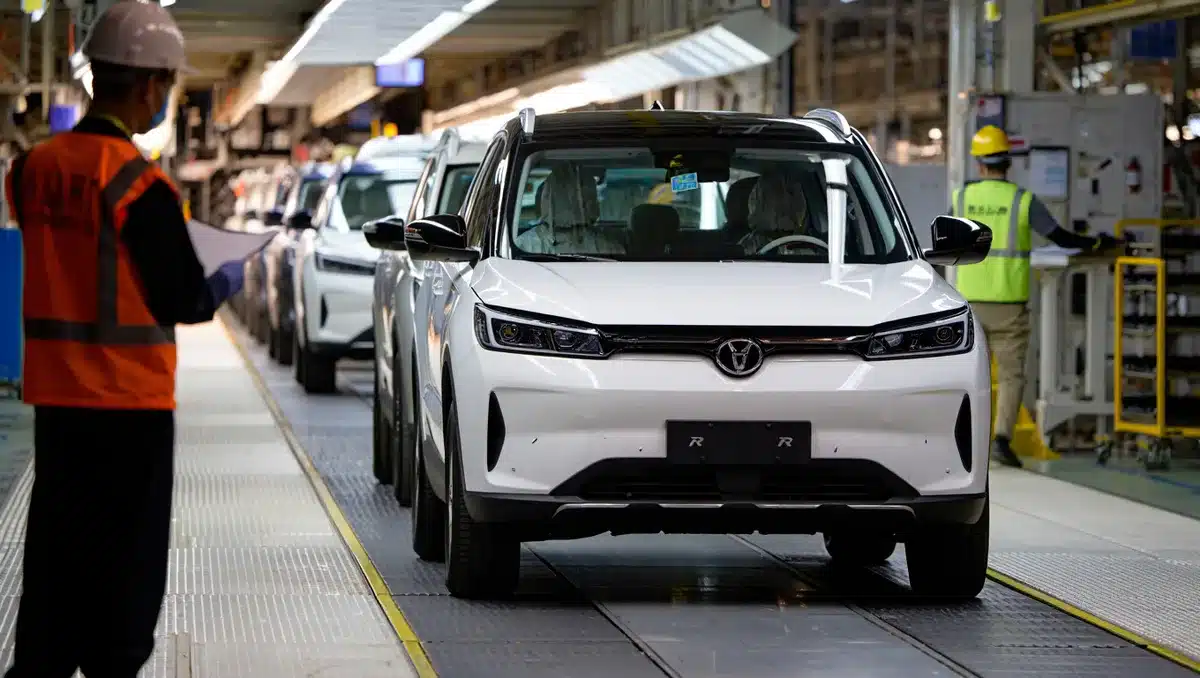 Electric vehicle production line with R2 SUVs moving through assembly stations, workers in safety gear monitoring quality checkpoints, industrial lighting illuminating the factory floor | vehicle assembly manufacturing