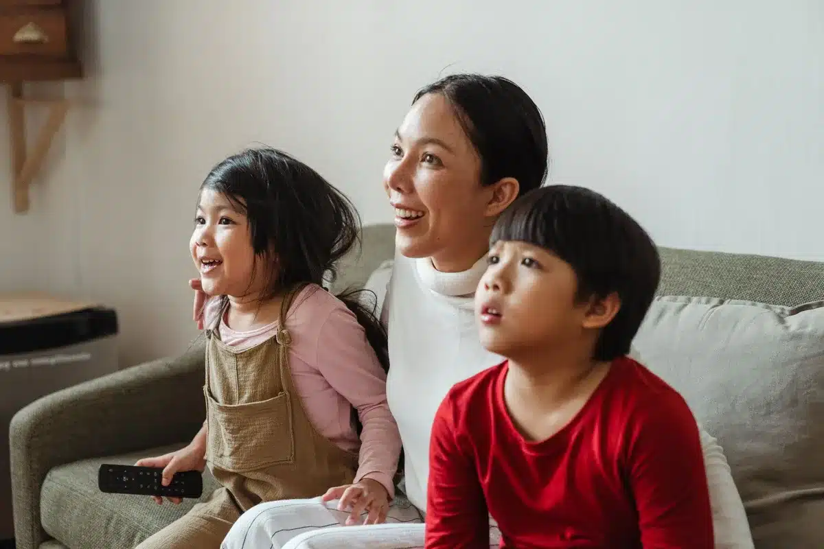 A diverse group of anonymous children in a living room looking at a television screen, with colorful cereal and snack food advertisements visible on the display, illustrating the current advertising environment the bill would restrict.