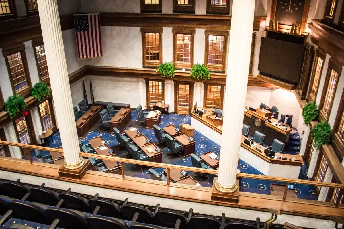 A divided Senate chamber floor with rows of empty desks, cool blue lighting casting shadows across the wooden surfaces, a single gavel on the presiding officer's desk catching light, tension and procedural gridlock evident