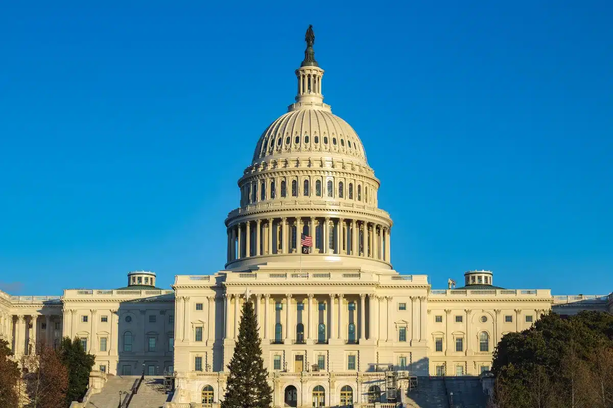 Capitol Building exterior at dusk, American flags hanging from the facade, Senate chamber windows illuminated, architectural detail showing classical columns
