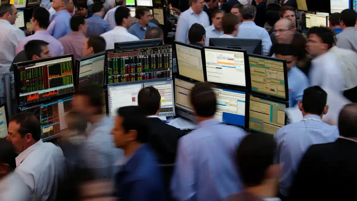 Stock market trading floor with multiple monitors displaying financial charts and data, traders in motion, representing real-time market reaction | stock market trading screens