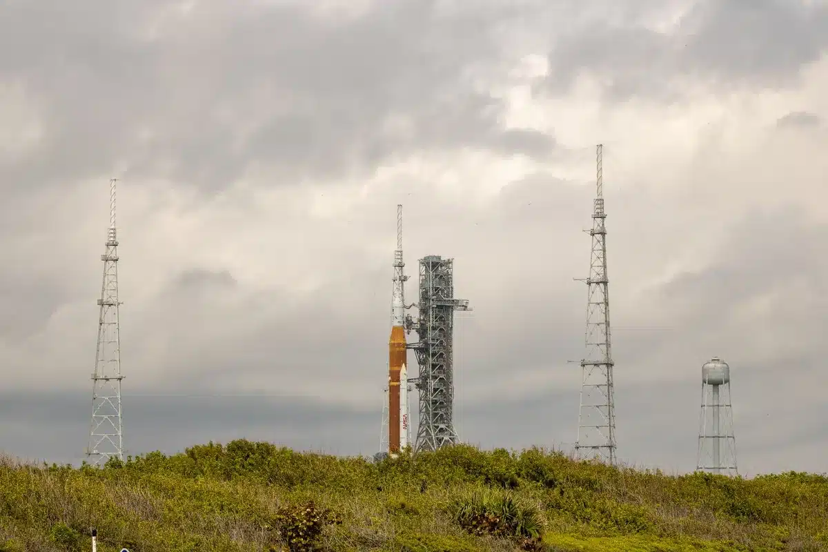 Starship rocket at launch pad before dawn, tall white vehicle against dark Texas sky, launch tower looming beside it, ground crew lights visible