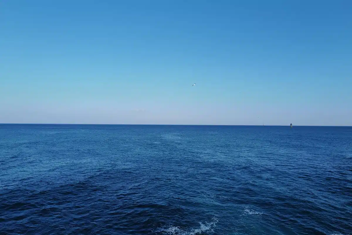 A spacecraft upper stage descending through Earth's atmosphere, trailing plasma and heat, ocean waves visible far below, the moment before water contact in tropical waters.