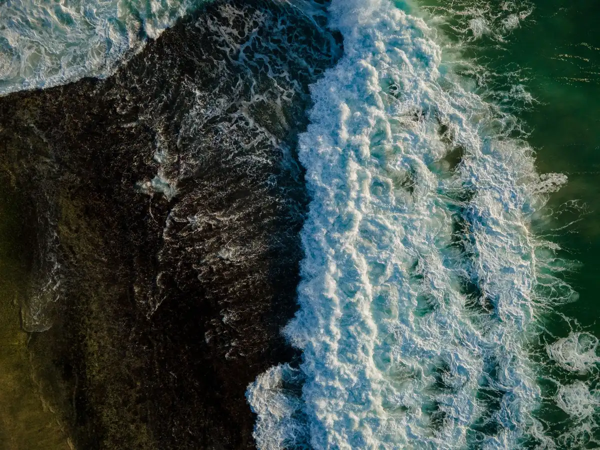 Starship spacecraft floating intact on ocean surface after splashdown, residual propellant flames visible, drone perspective from above, calm water surrounding intact vehicle