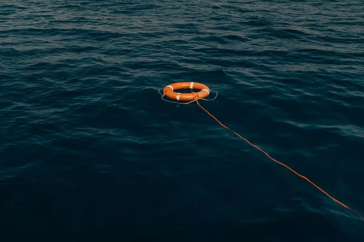 A glowing upper stage section floating in calm ocean waters, intact after splashdown, sunlight reflecting off the hull, recovery vessels visible at a distance.