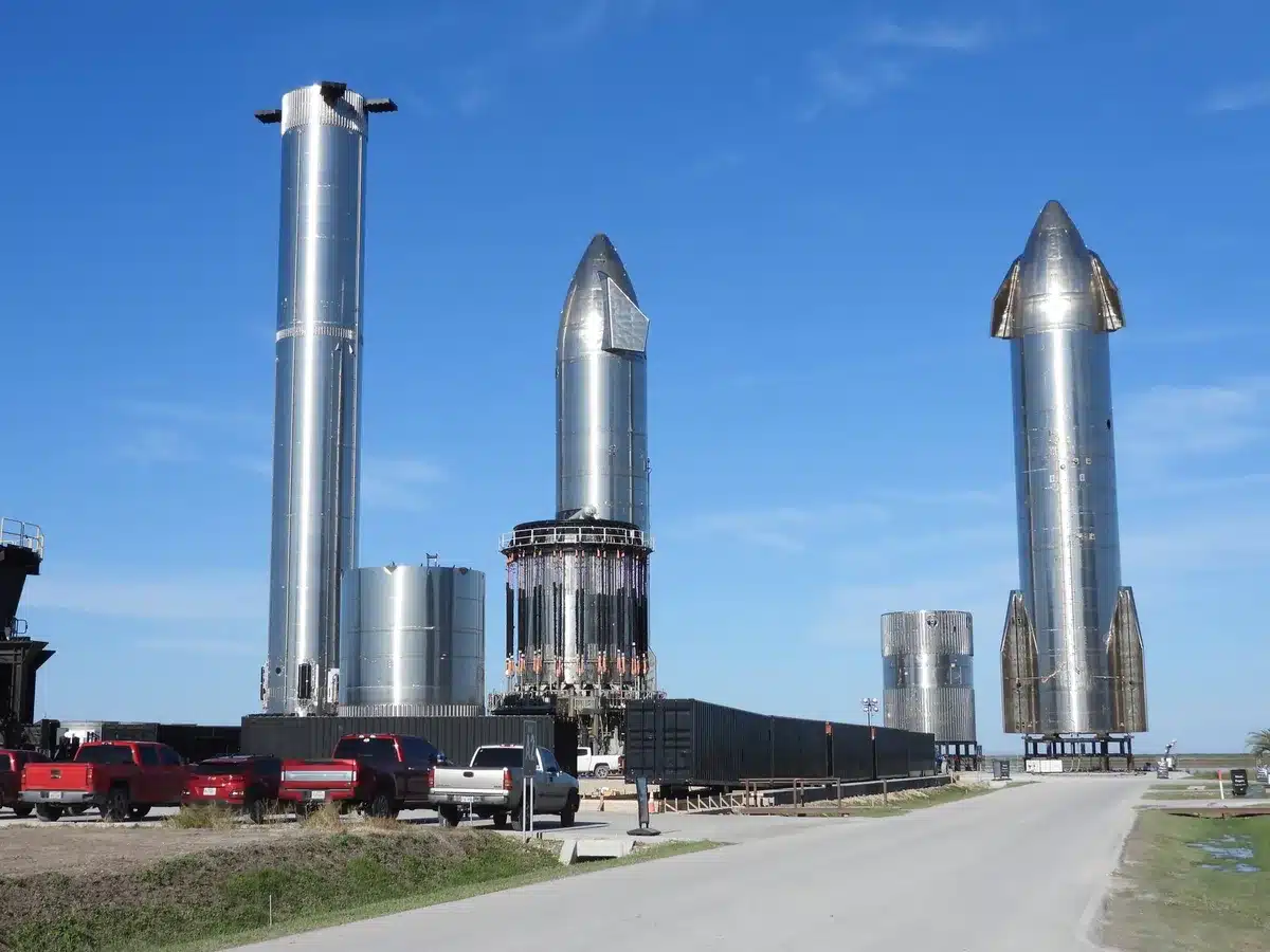 Starship's booster on the launch pad at Starbase, surrounded by the deluge system's water spray and support structures, dawn light breaking across the Texas landscape, anticipation.