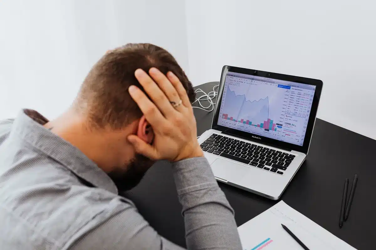Smartphone and computer screens displaying red stock market data, candlestick charts in sharp decline, amber and crimson color palette