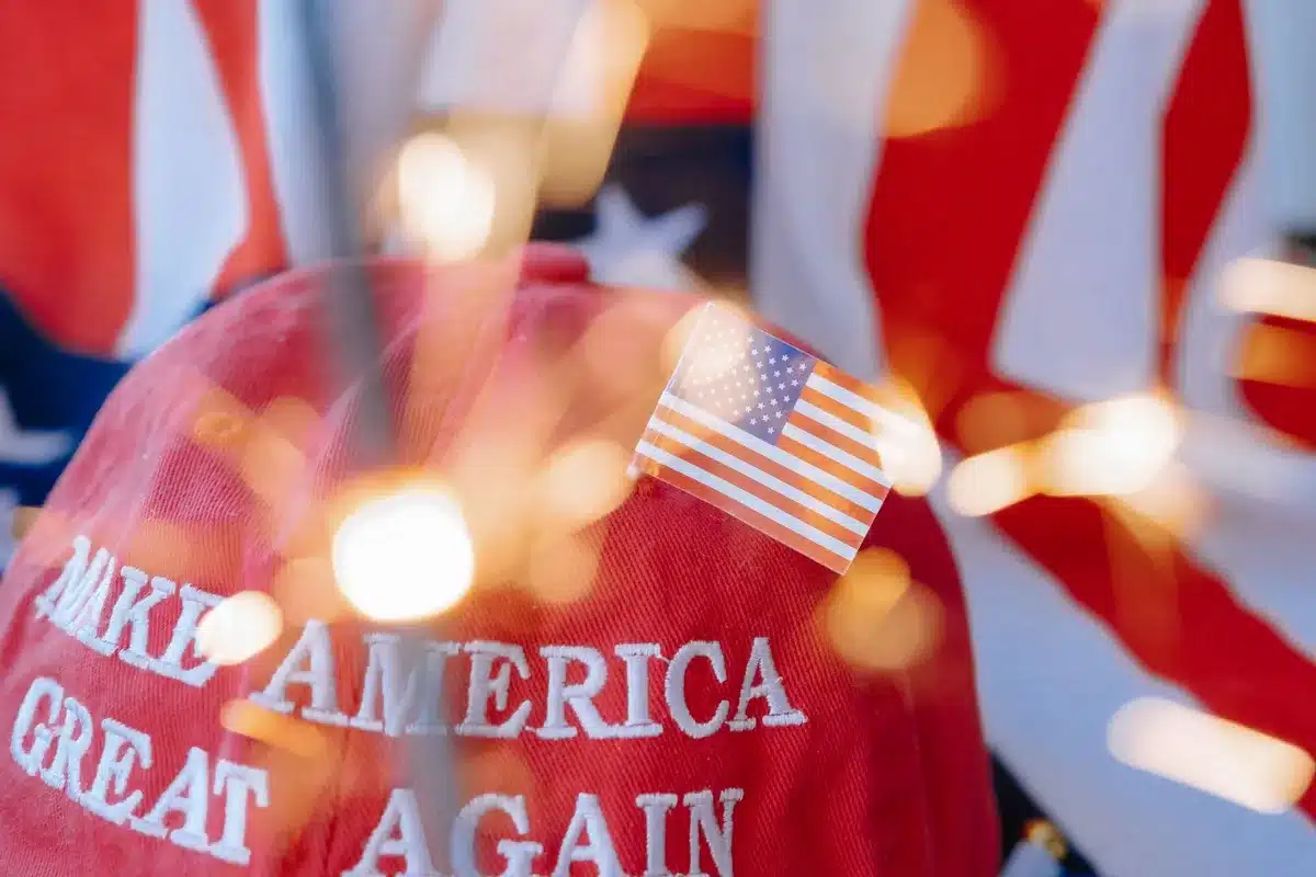 A close-up of a red baseball cap with "Trump 2028" embroidered in white lettering, lying on a dark polished table surface, a thin spotlight catching the embroidery detail, the background blurred and neutral.