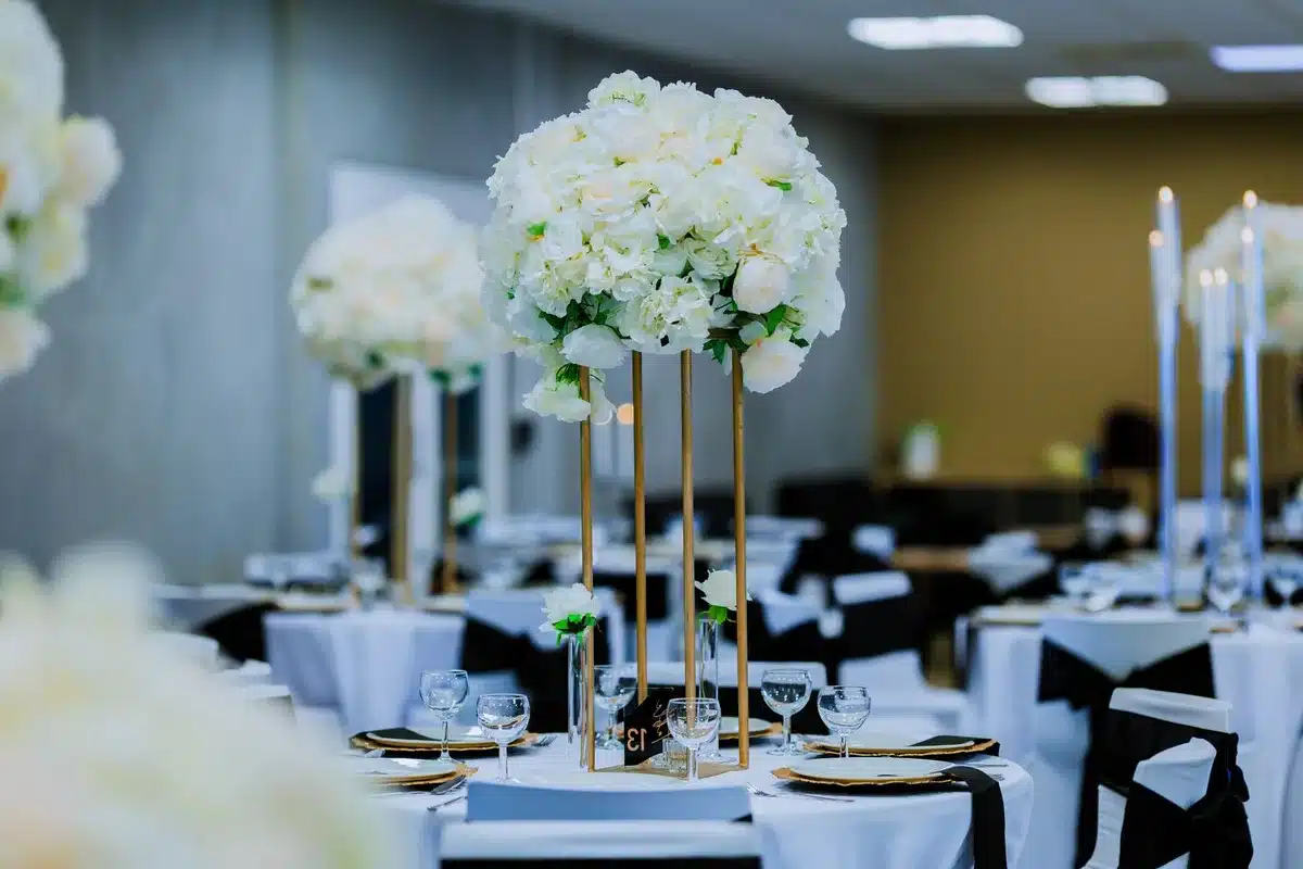 A formal ballroom setting with empty tables and elegant place settings, soft lighting casting shadows across white linens, a stage with a podium in the distance, no people visible, conveying anticipation and readiness.