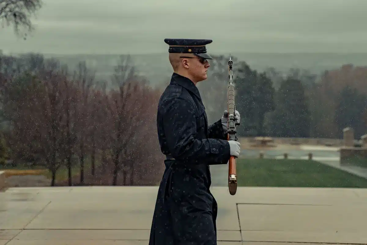 Military honor guard in dress uniforms standing at attention beside flag-draped transfer cases on an aircraft tarmac, solemn ceremony at dawn