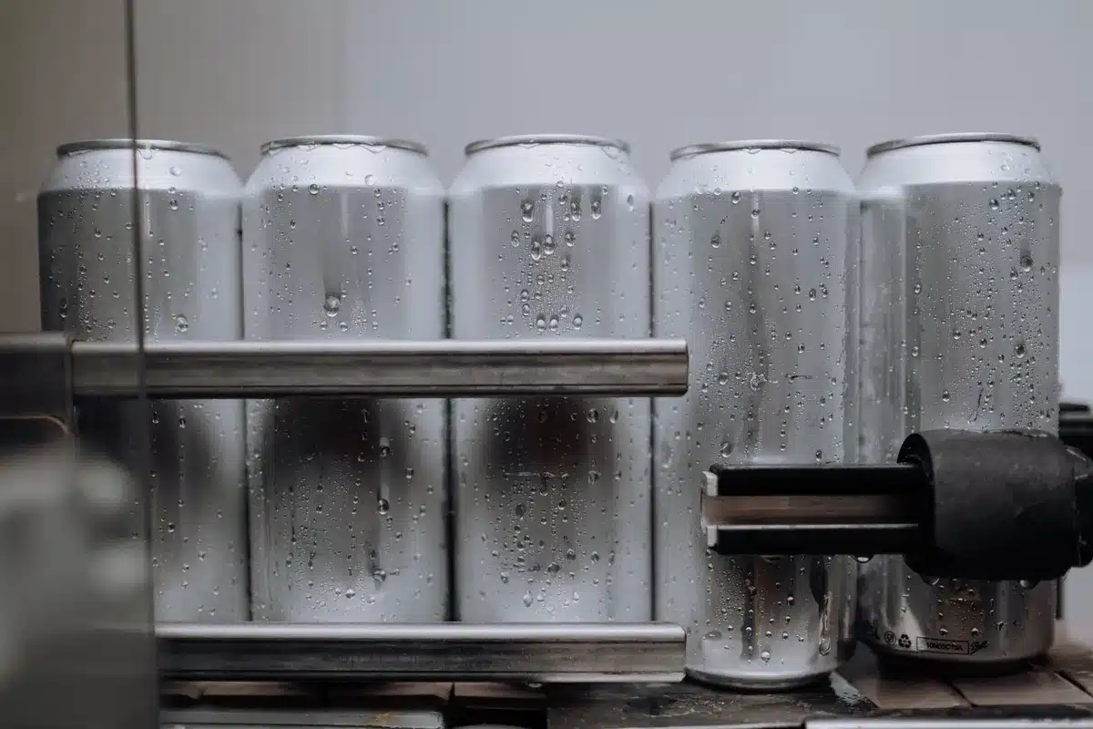 A beer can sitting alone on a dark surface with a harsh spotlight creating dramatic shadow, the can unlabeled and generic, suggesting corporate or consumer product in question