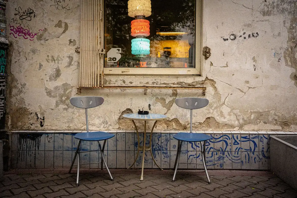 Two opposing empty chairs facing each other across a polished wooden table, tension visible in the stark composition, harsh overhead lighting casting sharp shadows between them