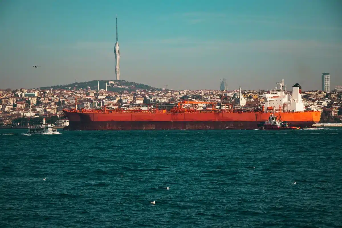 Oil tanker ships lined up in a port facility, industrial pipelines and storage tanks visible, crude oil export infrastructure under bright daylight, commercial maritime operations