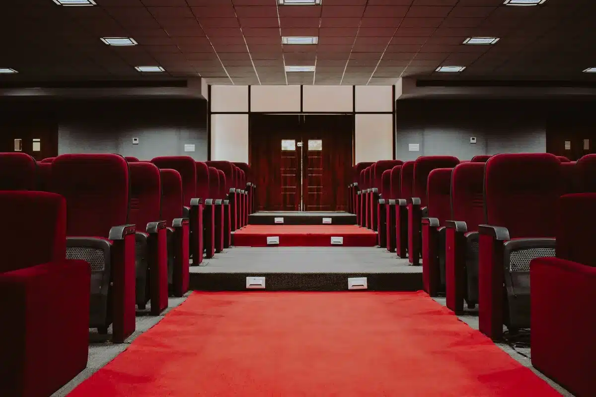 An empty podium on a stage with a single spotlight illuminating it, formal curtains in the background, the rest of the stage in shadow, suggesting anticipation and significance