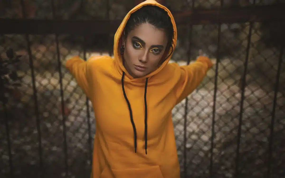 A cream-colored hoodie with bold text sits next to two open beauty kit boxes displaying colorful cosmetics and skincare products on a neutral background, arranged to show the full collaboration collection.