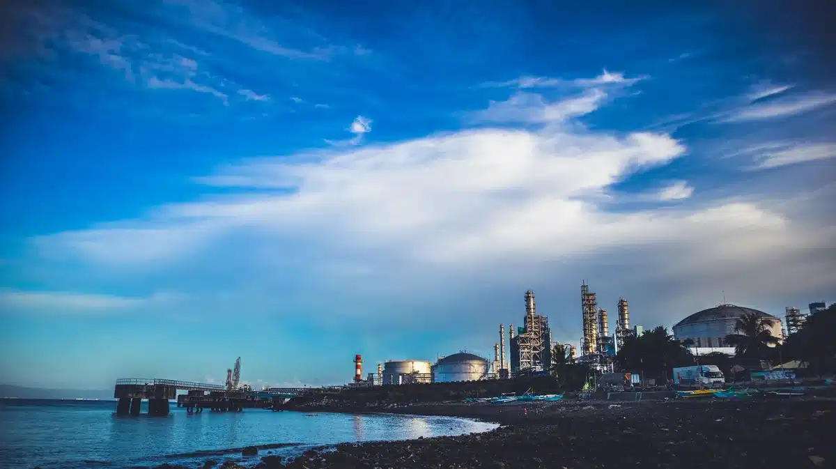 Oil refinery complex at dusk with multiple smokestacks and industrial structures against a darkening sky, no visible people, industrial landscape