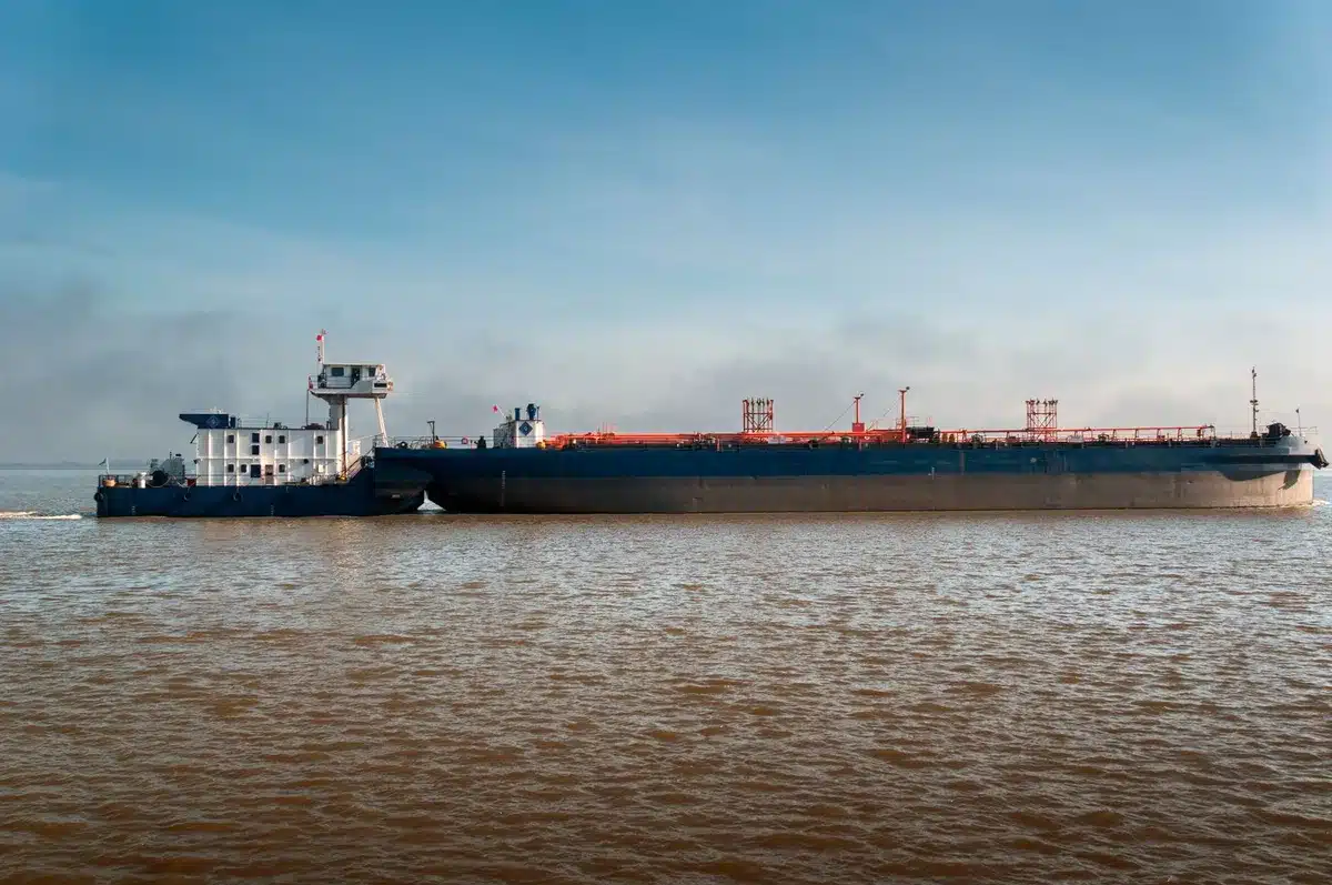 Container ship silhouette passing through narrow strait waters, distant military vessels on horizon, tension in the scene, economic vulnerability visible