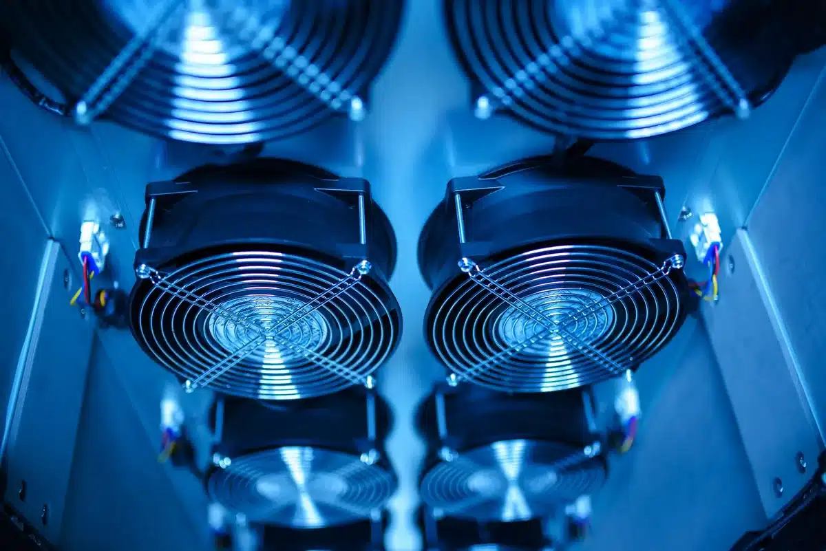 Data center filled with server racks and cooling infrastructure, blue and white LED lights illuminating rows of equipment, no people visible