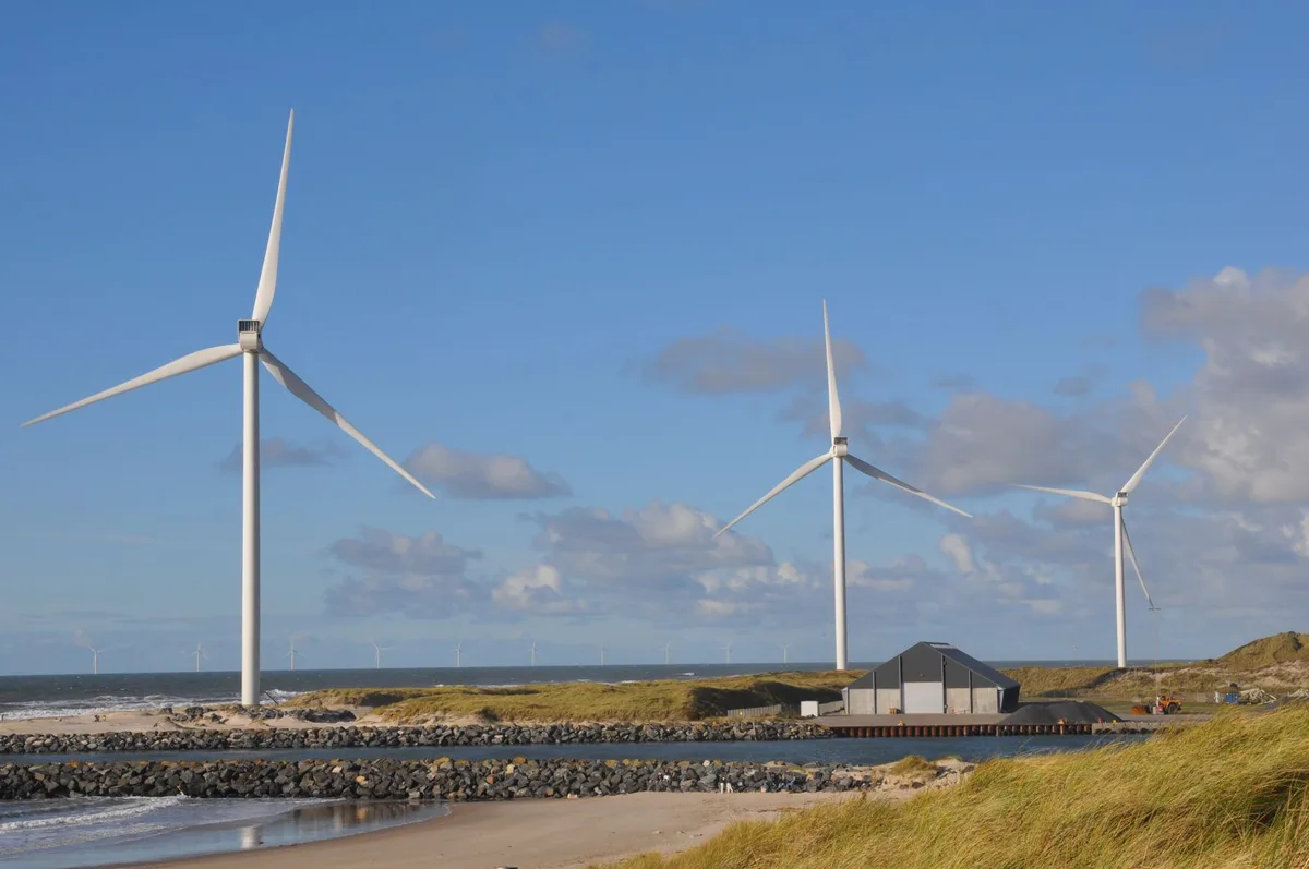 Construction cranes and turbine components at a wind farm site, workers in safety gear assembling foundations, multiple projects under simultaneous development, clear sky with white turbine towers rising, urgency and scale visible in the parallel construction activity