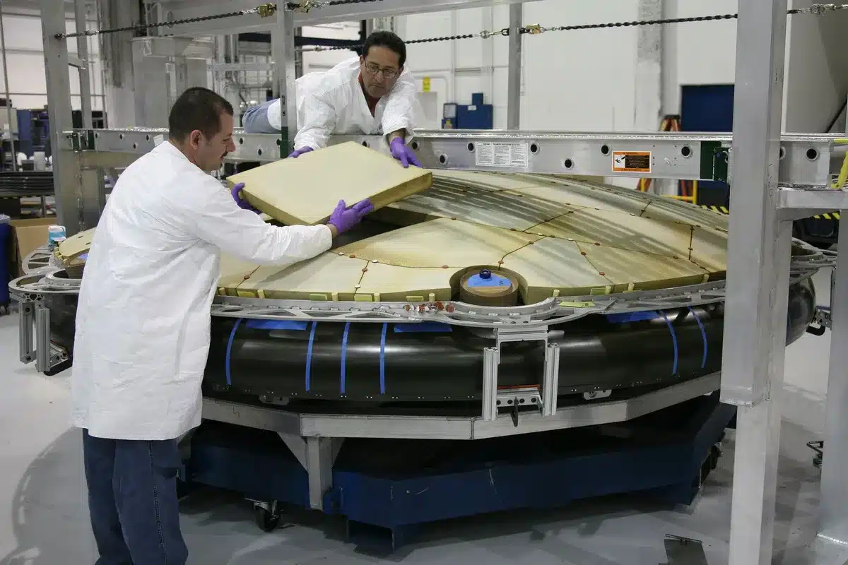 Modern semiconductor manufacturing facility with rows of optical equipment and testing stations, bright white LED work lights illuminating precision machinery, clean-room environment with anonymous technicians in protective gear working at stations, sense of industrial scale and precision