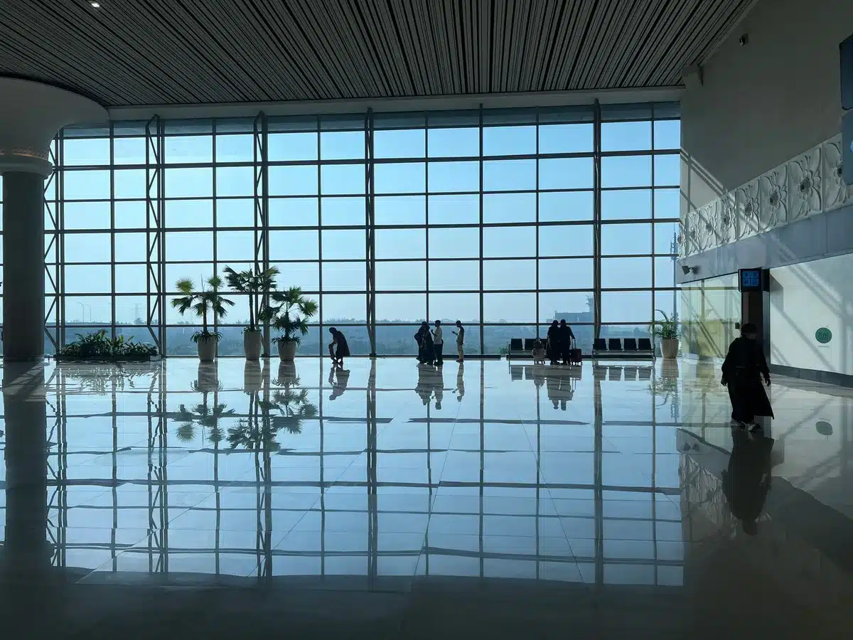 Busy airport terminal with prayer and washing facilities visible in background