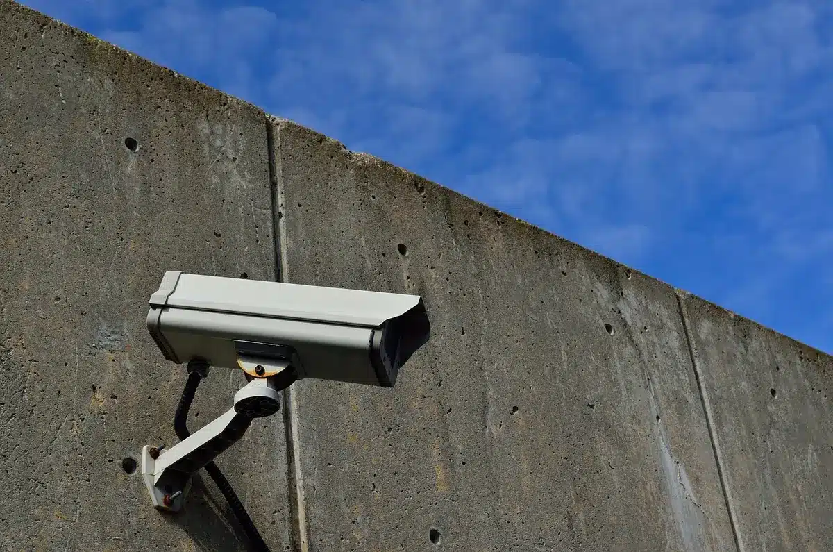 Police department building exterior at dusk, a single camera mounted on a pole nearby, surveillance equipment silhouetted against fading light, sense of law enforcement accountability and oversight