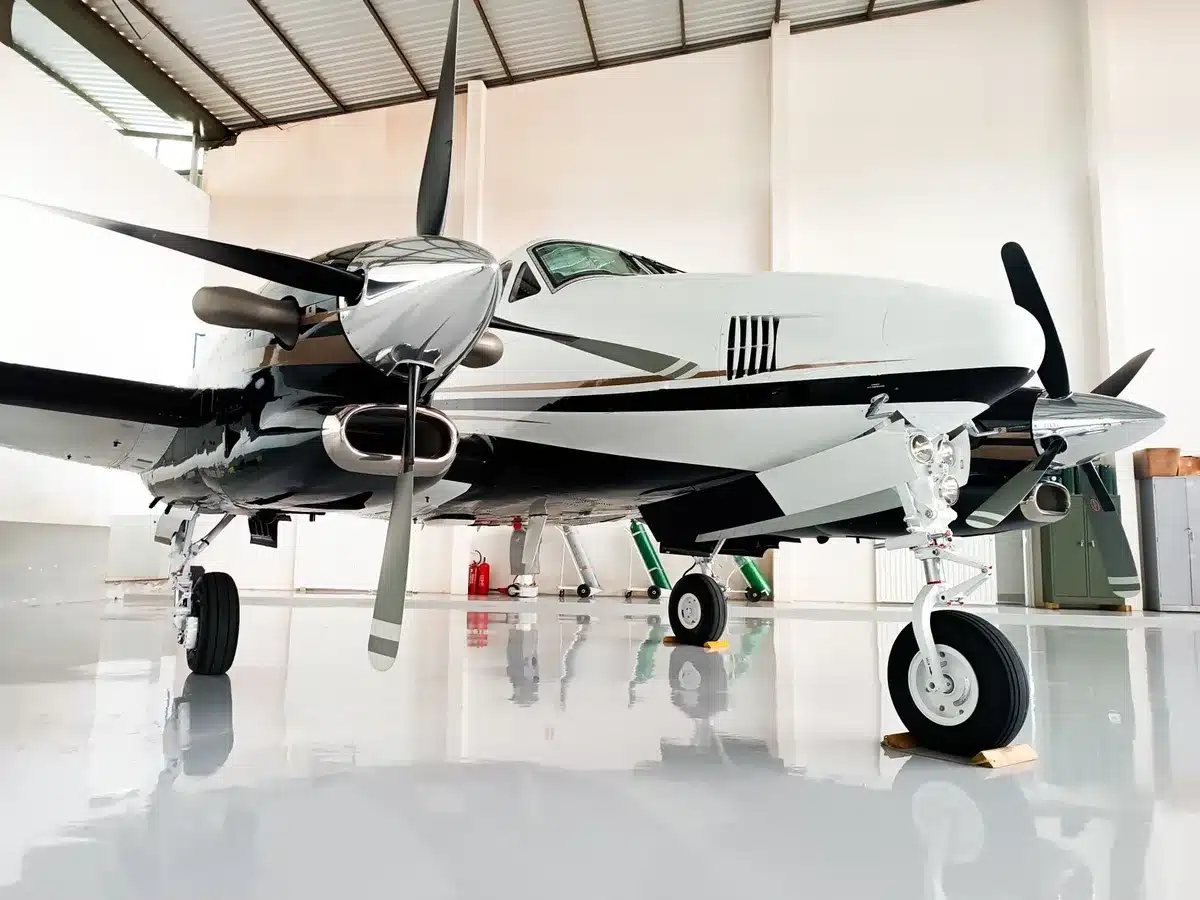 A modern aircraft hangar interior with a wide-body jet elevated on maintenance stands, technicians in safety gear working on cabin interior sections, disassembled aircraft components organized in work zones, industrial lighting illuminating the precision engineering work.
