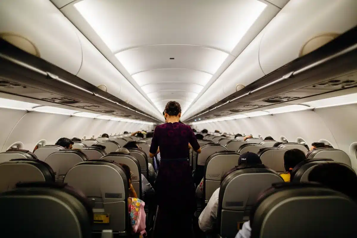A cross-section view of an aircraft cabin showing the upper deck with rows of Premium Economy seats in tan leather, the 2-3-2 configuration clearly visible, modern cabin lighting and overhead bins, a glimpse of the Business Class section below, modern finishes and wood accents.