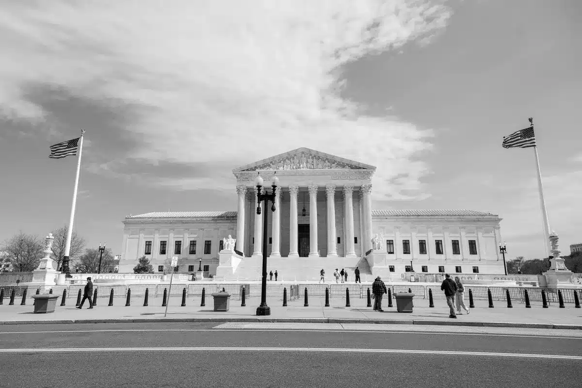 A marble-columned Supreme Court building interior, empty courtroom benches in soft morning light, a single gavel resting on the bench