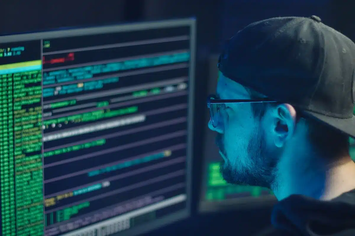 A computer security monitoring dashboard with red alert indicators, network topology diagrams, and threat detection logs scrolling across multiple screens in a darkened control center