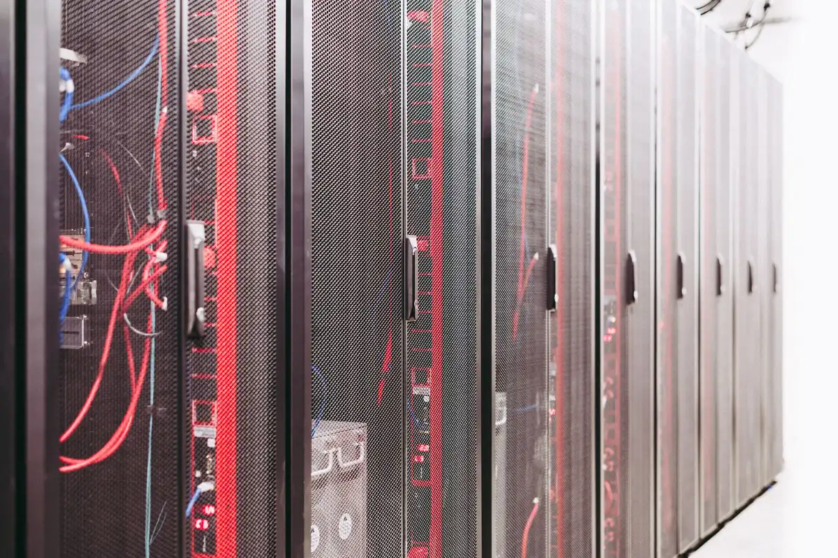 Data center server room with illuminated hardware racks and cables, blue and green indicator lights reflecting off organized infrastructure emphasizing computational scale.