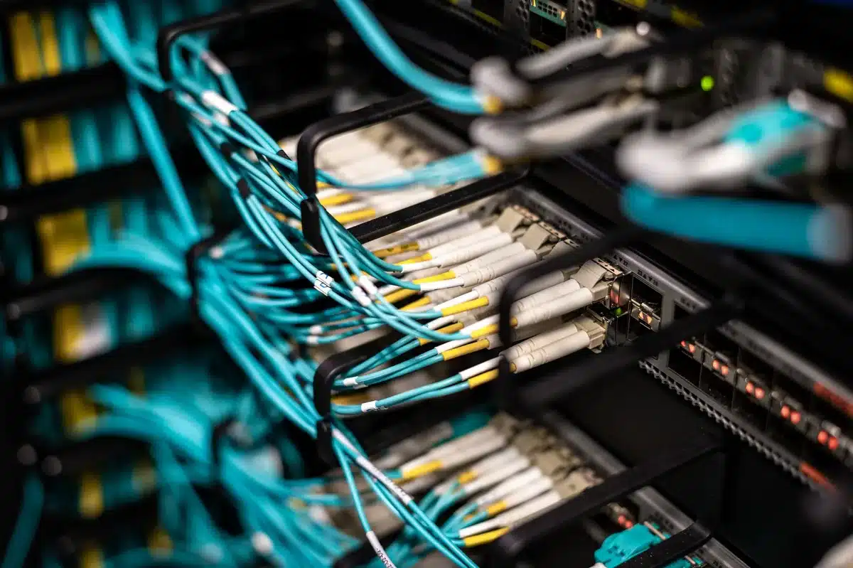 A modern data center server rack illuminated by cool blue light, with fiber optic cables glowing, showcasing dense GPU accelerator modules installed in the chassis.