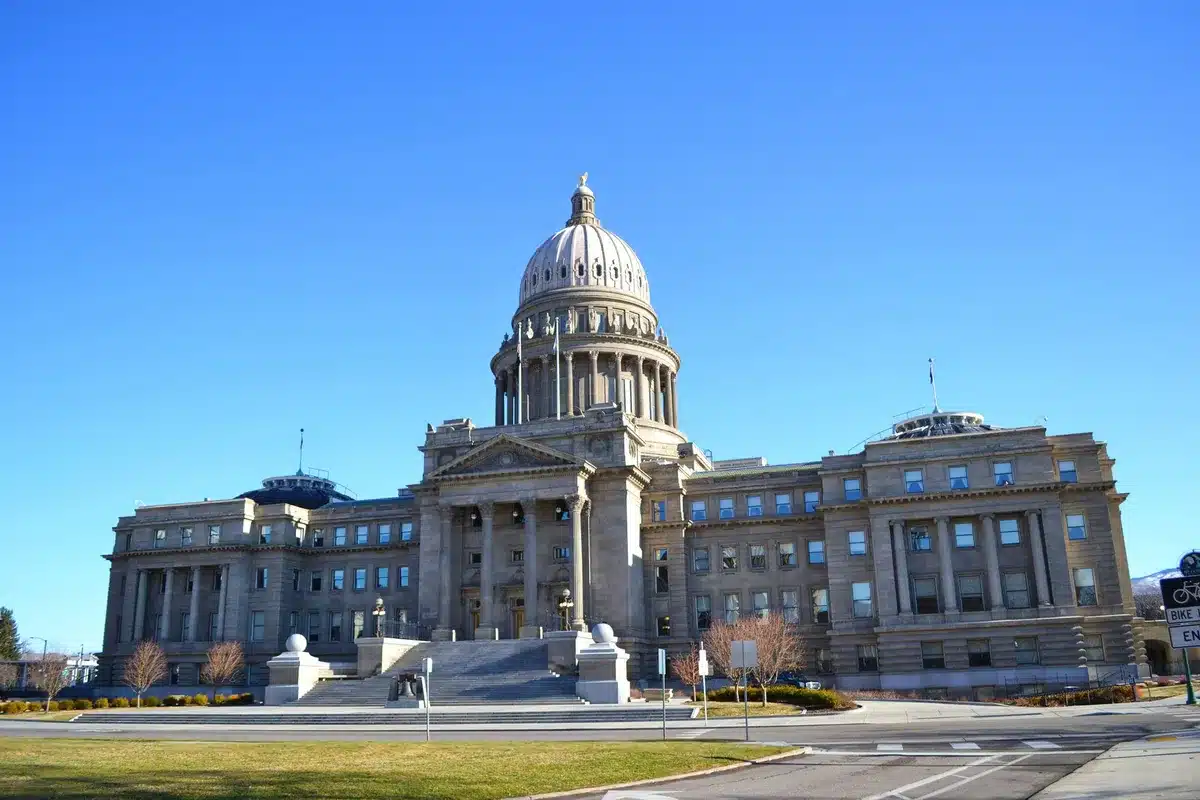 A state capitol building exterior with tax-related protest signs visible in the foreground, daytime, autumn lighting, architectural detail