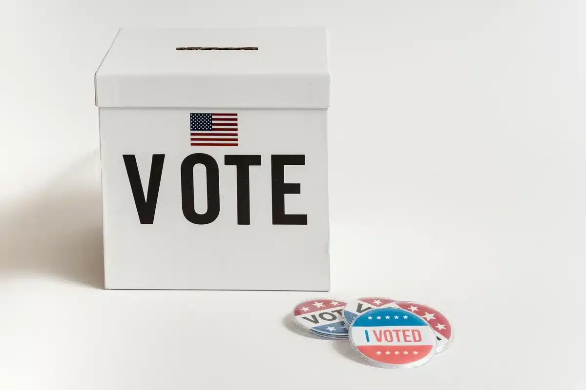 A voting booth in a Minnesota polling location, early morning light filtering through windows, an empty chair facing the ballot, quiet anticipation