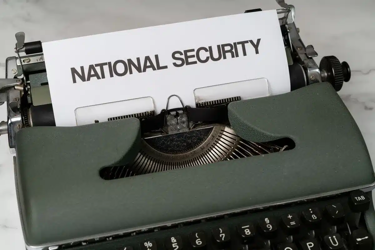A desk stacked with government forms, documents, and paperwork in neat piles, a pen resting on top, soft overhead light casting shadows on the papers.