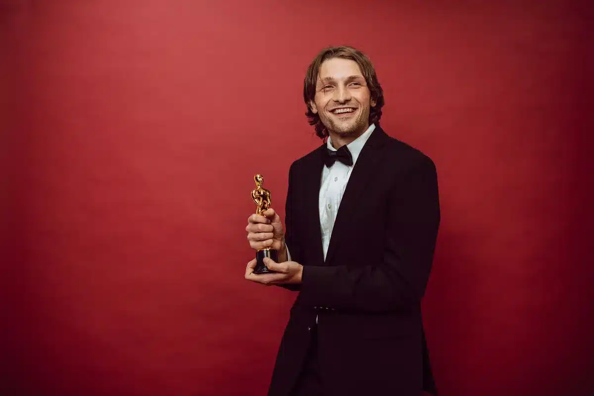 A spotlight illuminating an empty award podium on an elegant gala stage, gold confetti suspended mid-air, formal dinner tables blurred in the background, one gleaming crystal award on the top step catching warm light