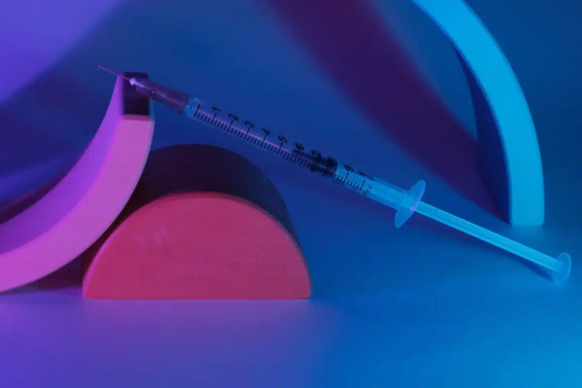A close-up view of a medical syringe with clear fluid, held at an angle against a blurred clinical background, sterile and clinical lighting emphasizing the precision of the moment.