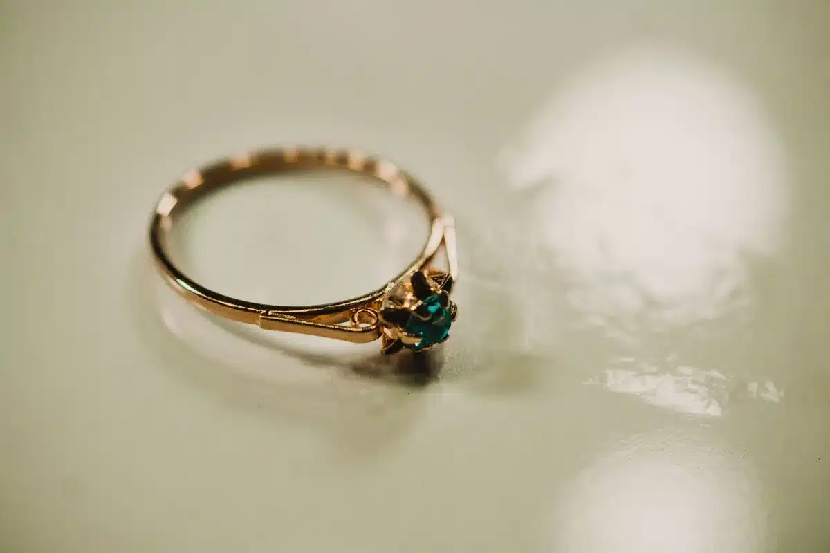 A couple's engagement ring sitting on a marble surface, catching soft light, the stone gleaming against the cool stone background, intimate and solitary.
