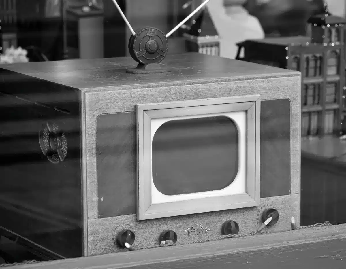 Vintage television set from 1960s with dark screen, analog dials visible, sitting in dim room with single spotlight creating dramatic shadow
