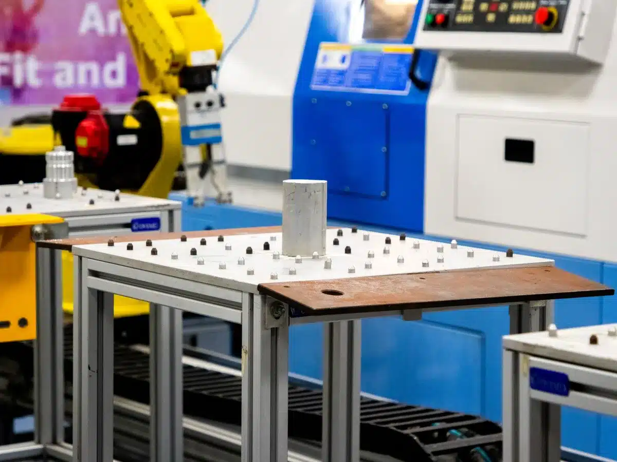 Sleek modern aerospace facility interior with aircraft assembly floor, blue and white industrial lighting, engineers in protective gear reviewing digital blueprints on tablets, polished metal surfaces reflecting light, sense of precision manufacturing and innovation