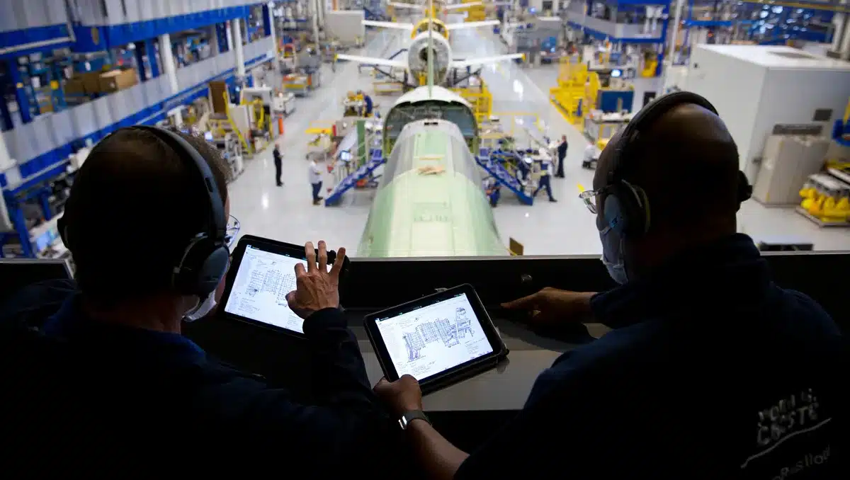 Sleek modern aerospace facility interior with aircraft assembly floor, blue and white industrial lighting, engineers in protective gear reviewing digital blueprints on tablets, polished metal surfaces reflecting light, sense of precision manufacturing and innovation | aerospace manufacturing facility