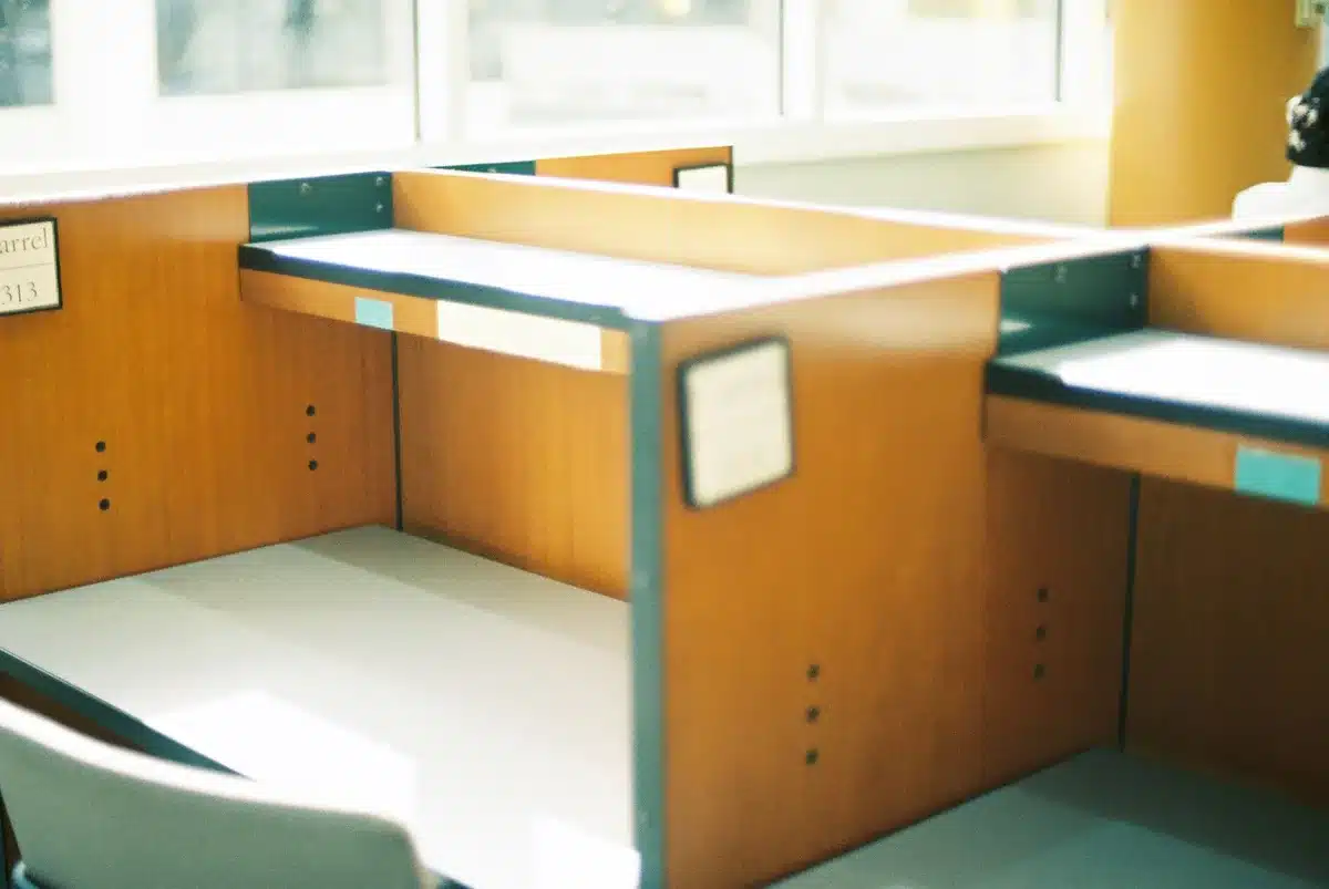 A modern newsroom with empty desk stations, computer monitors dark, chairs pushed back, fluorescent overhead lights casting shadows on vacant workspaces, editorial boards on walls in soft focus, one abandoned coffee mug on a desk
