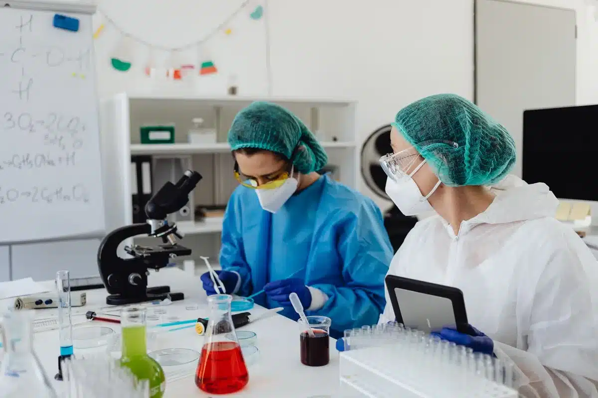 Two pharmaceutical research scientists in a modern laboratory examining molecular models and data displays, one pointing at a glowing screen showing molecular structures