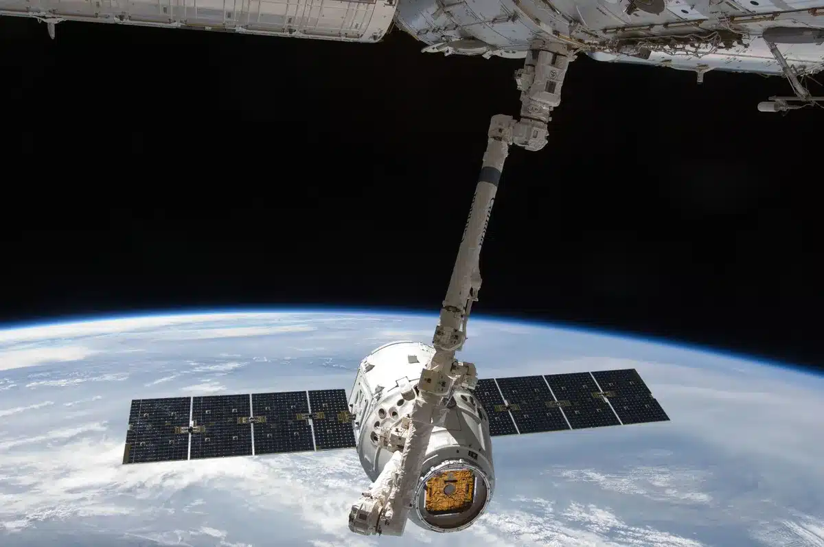 A satellite in orbit above Earth against a starfield, with solar panels extended, transmitting signals downward to a distant blue planet surface