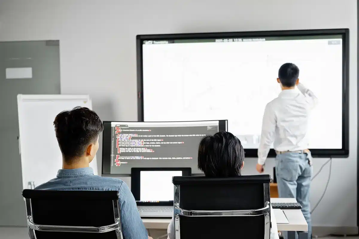 A sleek tech office workspace with developers collaborating around computers showing software development tools and dashboards, embodying modern enterprise software culture