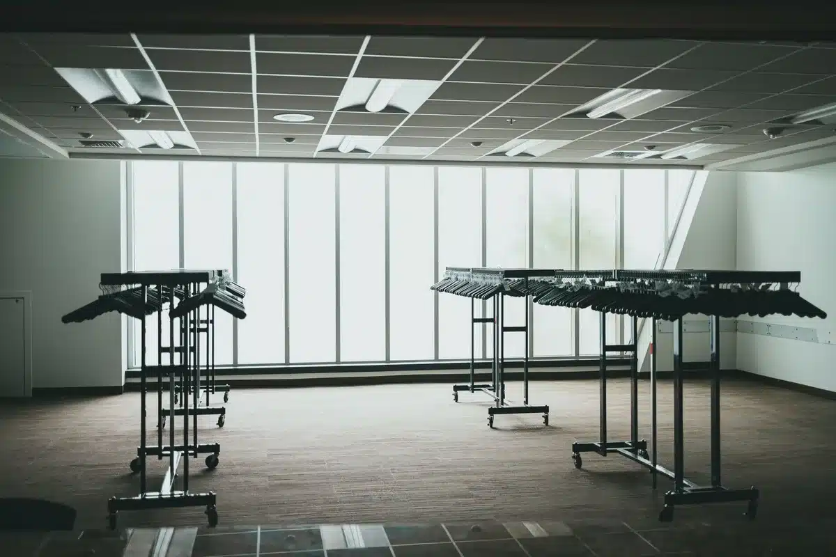 Empty retail showroom floor with dust particles visible in sunlight streaming through tall windows, abandoned furniture displays, no people present, a sense of stillness and closure