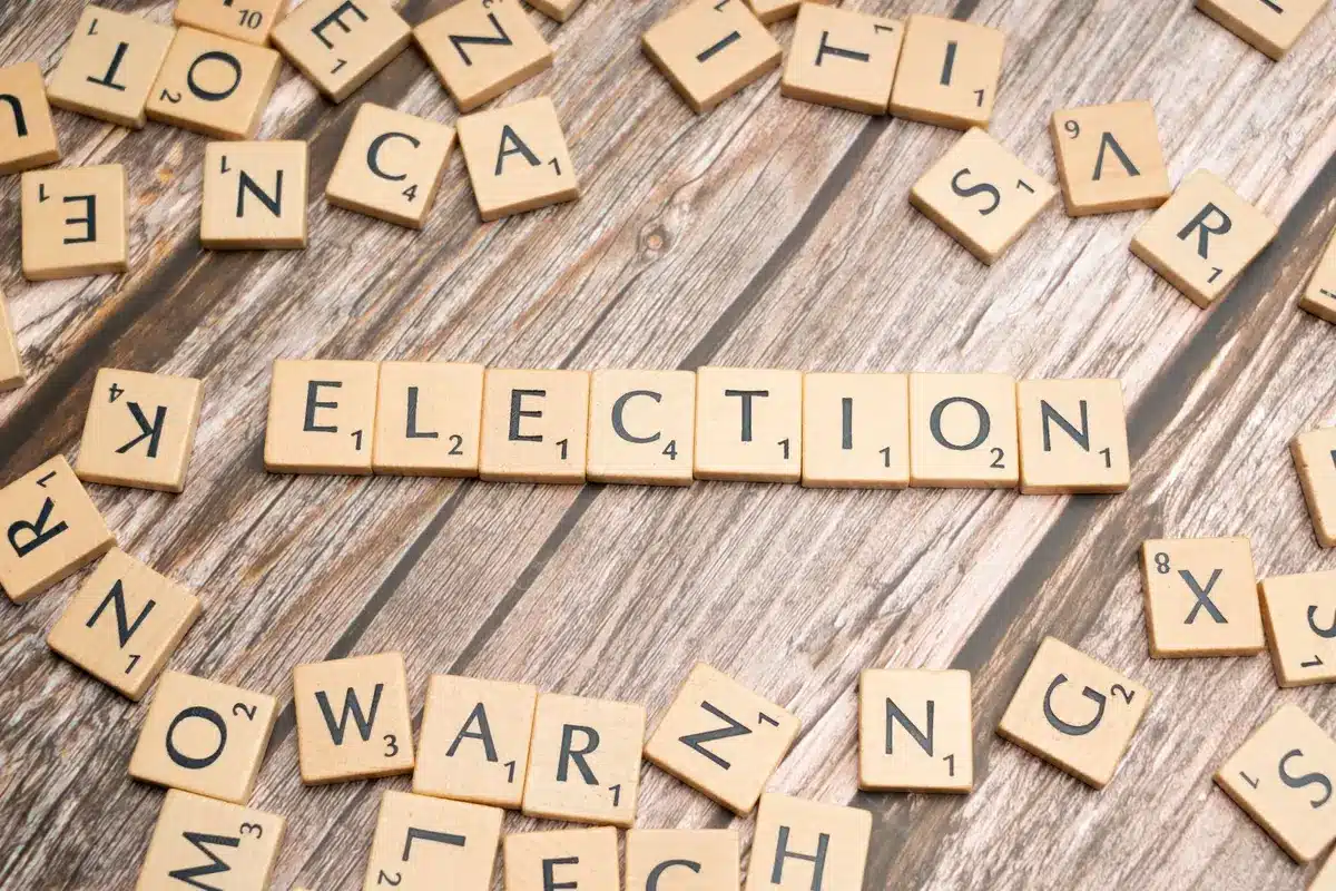 A crowded polling place with voters casting ballots at voting machines, diverse hands holding ballots, poll workers in background, democratic participation in action.