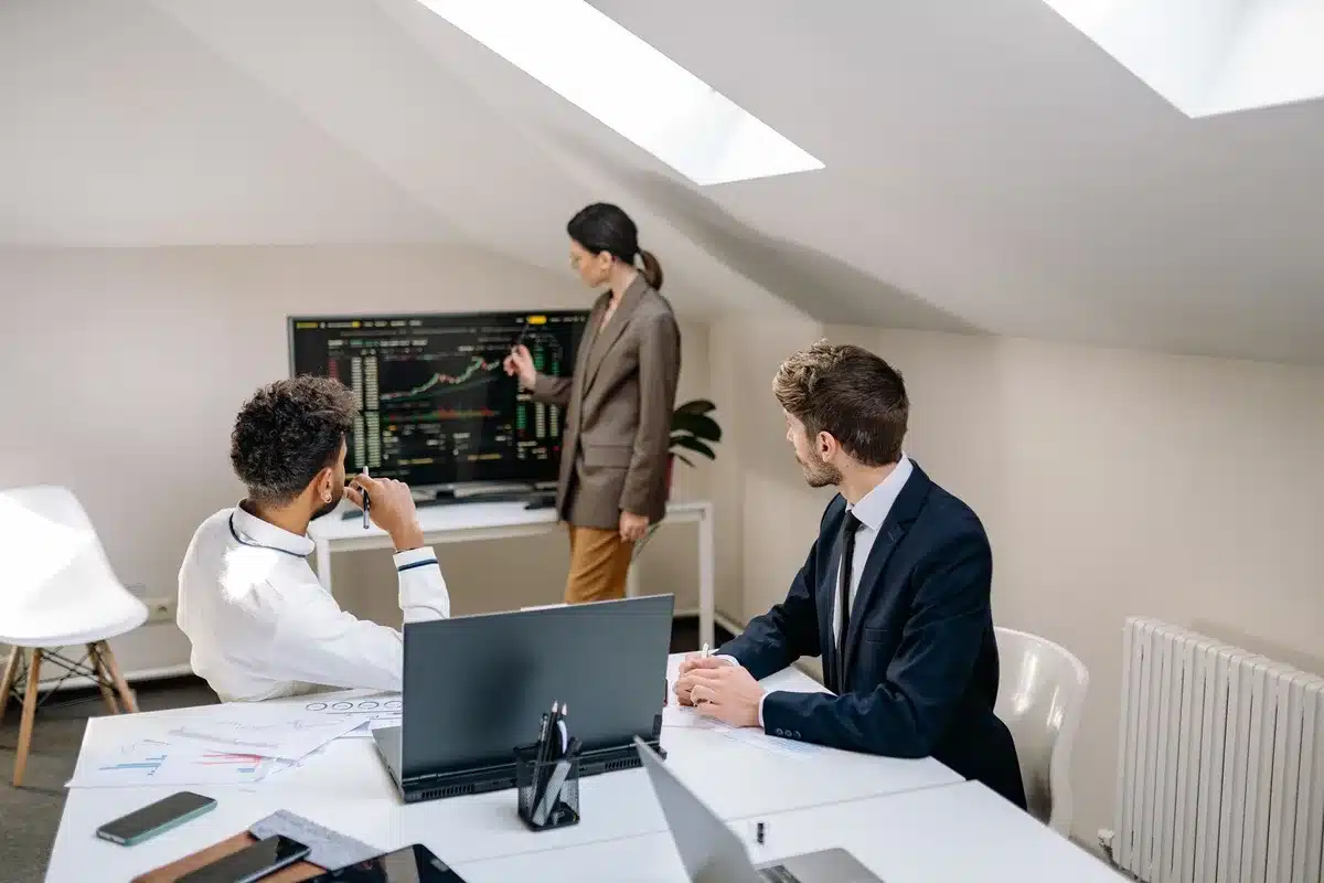 A modern office boardroom with a large mahogany table, Bloomberg terminal screens displaying financial data and stock tickers, morning sunlight streaming through floor-to-ceiling windows overlooking a cityscape, an empty CEO chair at the head of the table, papers and reports scattered across the surface.