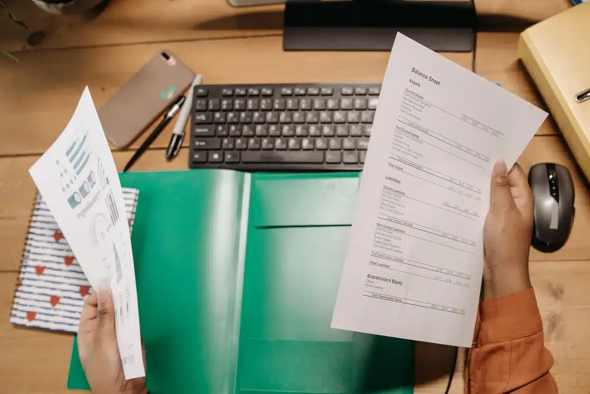 A sleek glass and steel skyscraper interior, a close-up of hands holding a financial report or earnings statement, soft focus on the document's header with "Berkshire Hathaway" visible, blurred stock market data on a secondary screen in the background, cool blue and gray tones.