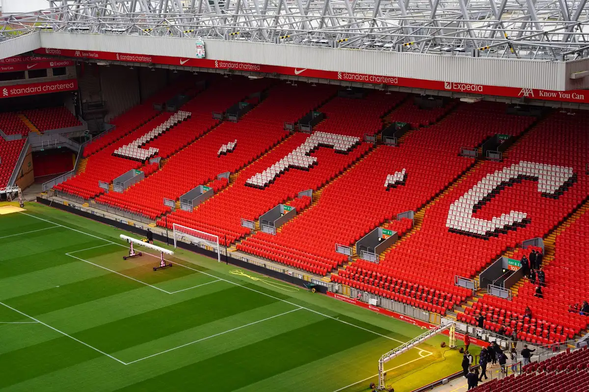 Anfield stadium exterior at dusk with warm floodlights illuminating the iconic structure, no crowds visible, quiet architectural moment conveying heritage and transformation